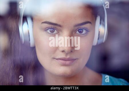 Porträt einer jungen Frau hinter dem Fenster Musik hören mit Kopfhörern Stockfoto