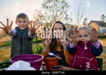 Portrait der Mutter mit zwei Kindern, die ihre schmutzigen Hände vom Garten zeigen Stockfoto