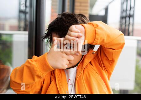 Nahaufnahme eines Jungen, der durch die Hände schaut, während er am Fenster steht Stockfoto