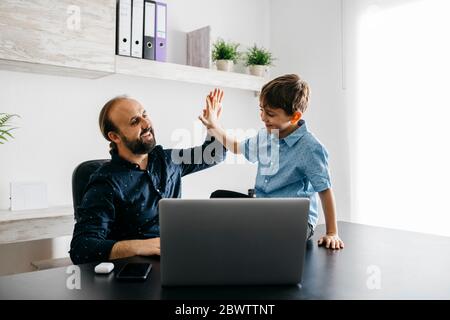 Glücklicher Vater High Fiving mit Sohn am Schreibtisch Stockfoto
