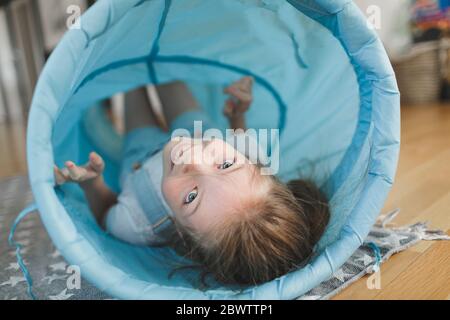 Lächelndes Mädchen spielt mit blauen Stoff Tunnel zu Hause