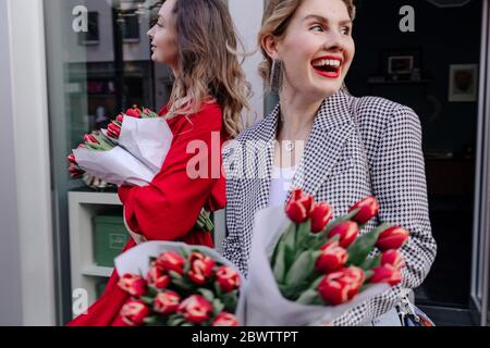 Zwei Frauen verlassen einen Blumenladen mit roten Tulpen Stockfoto
