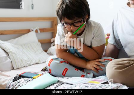 Junge lesen Arbeitsbuch während sitzen mit Vater auf dem Bett zu Hause Stockfoto