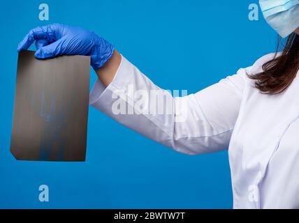 Doktor in einem weißen Mantel und blaue Latexhandschuhe halten eine Röntgenaufnahme der Hand eines Mannes und führen eine visuelle Untersuchung durch, weißer Hintergrund Stockfoto