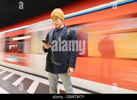 Stilvoller Mann mit Smartphone und Ohrhörer in der U-Bahn-Station Stockfoto