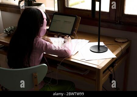 Mädchen mit Kopfhörern, die Manga-Comics zeichnen, während sie einen Tablet-Computer am Schreibtisch im Haus benutzen Stockfoto