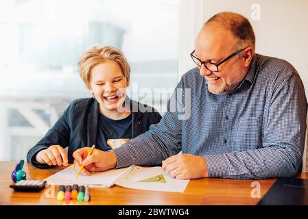 Glücklicher Vater und Sohn machen Hausaufgaben am Schreibtisch Stockfoto