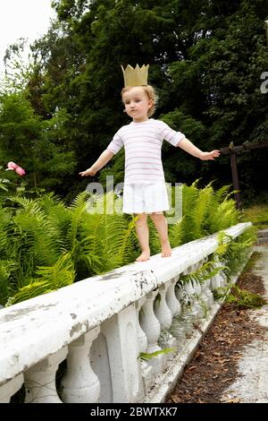 Kleines Mädchen, das auf einer Balustrade mit Pappkrone läuft Stockfoto