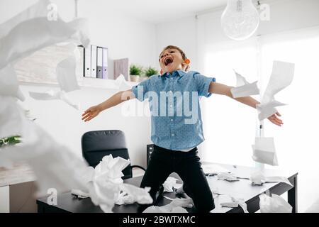 Schelmische Junge spielt mit Toilettenpapier auf dem Schreibtisch im Home Office Stockfoto