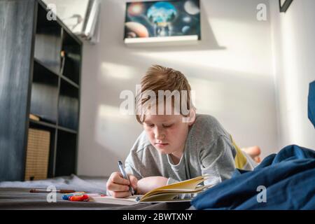 Portrait des Zeichnens Junge auf dem Bett zu Hause liegen Stockfoto