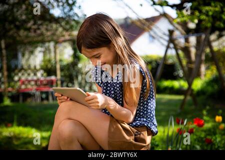 Happy girl sitzt im Garten mit digitalen Tablet Stockfoto