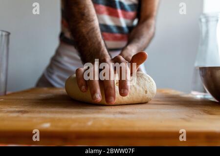 Hand des Mannes Kneten Teig auf Holzbrett, Nahaufnahme Stockfoto
