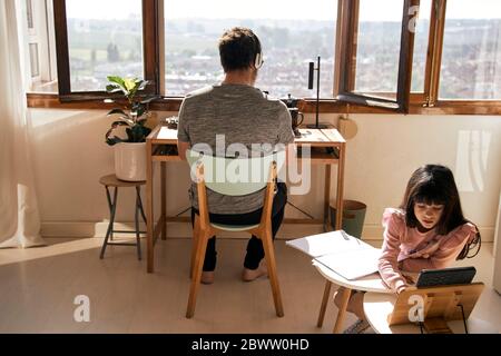 Mädchen macht Hausaufgaben, während ihr Vater auf Laptop im Hintergrund arbeitet Stockfoto