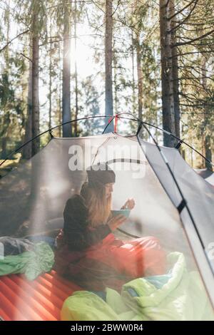 Junge Frau sitzt im Zelt, Frühstück im Wald Stockfoto