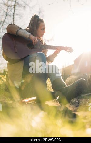 Junge Frau spielt Gitarre im Garten in Sonnenschein Stockfoto