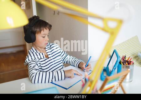 Junge tun Homeschooling und Schreiben auf Notebook, mit Tablet und Kopfhörer zu Hause Stockfoto