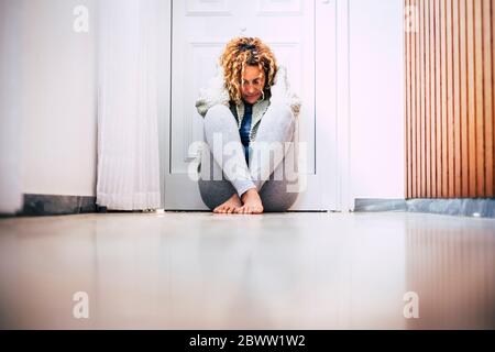 Verzweifelte Frau, die auf dem Boden im Flur vor der verschlossenen Tür sitzt Stockfoto