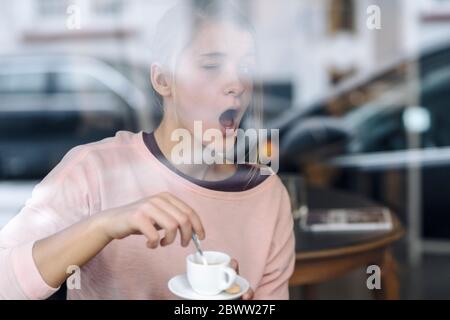 Porträt einer jungen Frau, die hinter einem Fensterscheibe in einem Café Grimassen Stockfoto