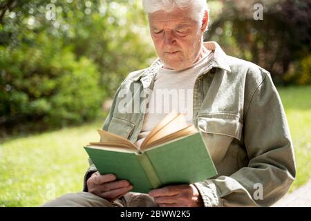 Rentner älterer Mann, der Roman liest, während er im Hinterhof sitzt Stockfoto