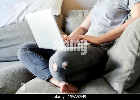 Niedriger Teil der Freiberufler mit Laptop, während auf dem Sofa zu Hause sitzen Stockfoto