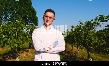 Junge Agronomen oder Biologen, die am Apfelbaum arbeiten, schreiben Tests in einem Notizbuch, in weißen Mänteln, Gummihandschuhen, dna, Schutzbrillen, Blatttests. Stockfoto