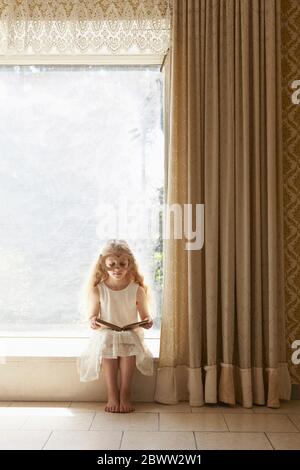 Mädchen auf Fensterbank sitzend, trägt Pappgläser Lesebuch Stockfoto