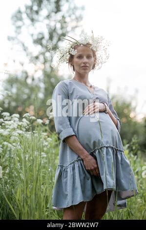 Portrait einer schwangeren Frau mit den Händen auf dem Bauch im Park stehend Stockfoto