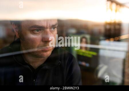 Porträt eines besorgten reifen Mannes, der am Abend aus dem Fenster schaut Stockfoto