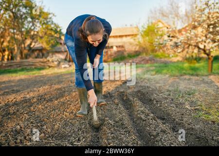 Volle Länge der Frau mit Hand Pflug auf dem Boden während der Gartenarbeit am Wochenende Stockfoto