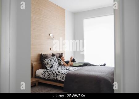 Frau, die nach dem Training zu Hause mit dem Smartphone auf dem Bett lag Stockfoto