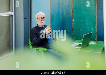 Porträt eines älteren Mannes, der mit einem Laptop im Freien sitzt und eine Pause hat