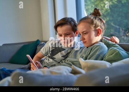 Bruder und Schwester sitzen zu Hause auf der Couch mit dem Smartphone Stockfoto