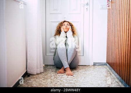 Verzweifelte Frau, die auf dem Boden im Flur vor der verschlossenen Tür sitzt Stockfoto