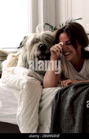 Lachende reife Frau auf dem Bett liegend und mit ihrem Hund spielend Stockfoto