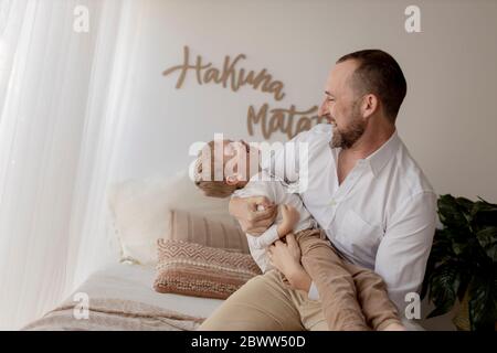 Vater hockend auf dem Bett kitzelt seinen kleinen Sohn Stockfoto