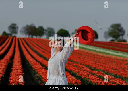 Porträt einer lächelnden Frau mit rotem Hut vor dem Tulpenfeld Stockfoto