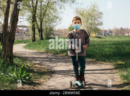 Portrait des Jungen trägt Schutzmaske mit Kick Scooter in einem Park Stockfoto