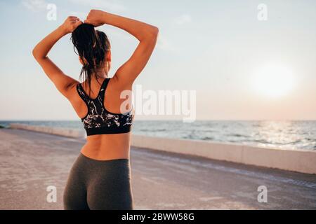 Rückansicht der jungen Sportlerin, die Haare bindet, während sie auf der Promenade steht Stockfoto