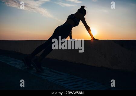 Silhouette Frau tun Liegestütze an der Promenade während Sonnenaufgang Stockfoto