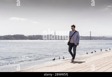 Junger Mann, der am Wasser mit dem Handy läuft Stockfoto