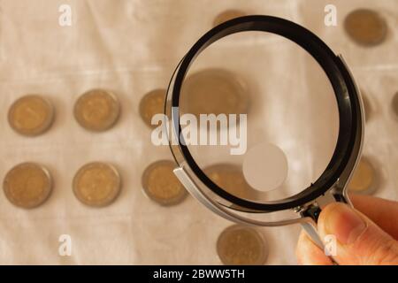Mann Hand mit Lupe und Blick auf zwei Euro-Münzen auf einem Tisch. Kopierbereich. Stockfoto