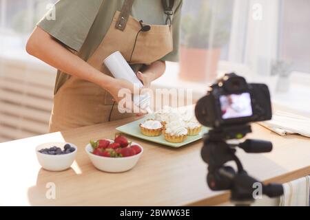 Nahaufnahme der Frau, die gebackene Kuchen mit Sahne dekorieren und den Videoinhalt in der Küche drehen Stockfoto