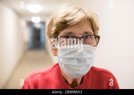 Ältere Frau mit Schutzmaske im Flur des Altenheims Stockfoto