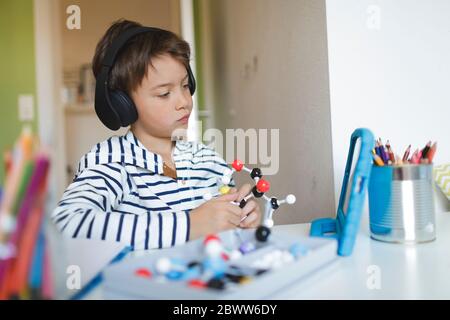 Junge tun Homeschooling und halten Molekül Modell, mit Tablet und Kopfhörer zu Hause Stockfoto