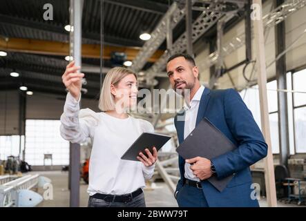 Geschäftsmann und junge Frau mit Tablet in einer Fabrik reden Stockfoto