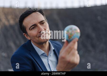 Reifer Geschäftsmann hält eine Miniatur-Globus auf einer stillgehaltener Mine Spitze Stockfoto