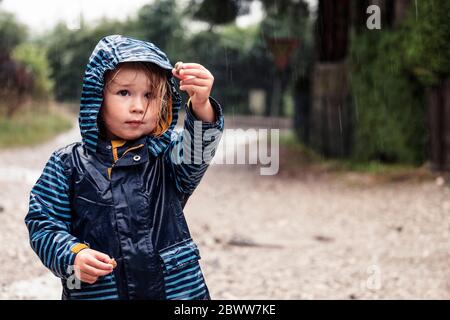 Portrait eines kleinen Mädchens mit Schnecken in den Händen, die im Regen stehen Stockfoto