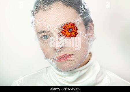 Portrait einer jungen Frau mit weißem Schleier und Blume, die ein Auge bedeckt Stockfoto