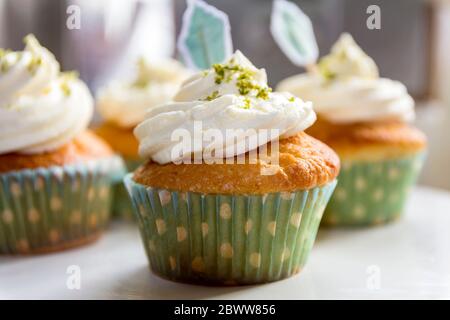 Tasse Kuchen mit Limettenglasur und Limettenschale auf dem Sahnehäubchen und Kuchenfahnen Stockfoto