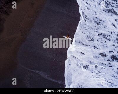 Indonesien, Bali, Pererenan Beach, Luftaufnahme des eineinmaligen Surfers am schwarzen Küstenstrand Stockfoto